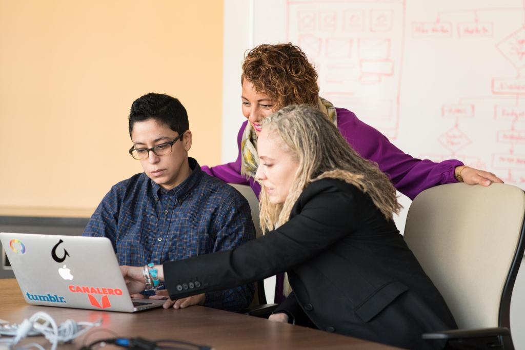 Three people look at a computer.