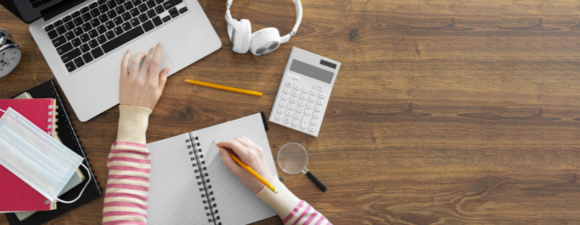 Person working at a desk with pen, paper, and a laptop.